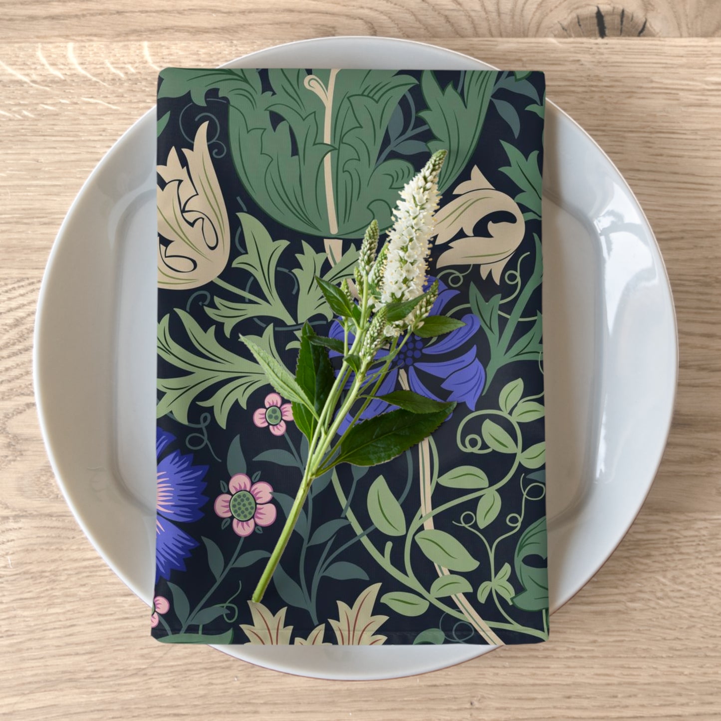 A floral patterned cotton twill napkin inspired by William Morris, displayed on a plate with a piece of floral decor.