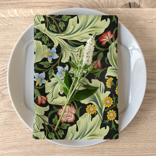 A green cotton twill napkin with a floral design by William Morris, placed on a plate on a wooden table.