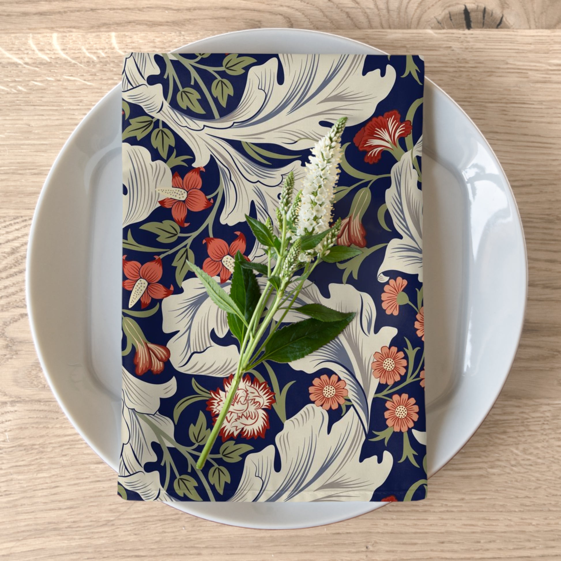 A floral patterned cotton twill napkin inspired by William Morris, displayed on a plate with a white flower decoration.