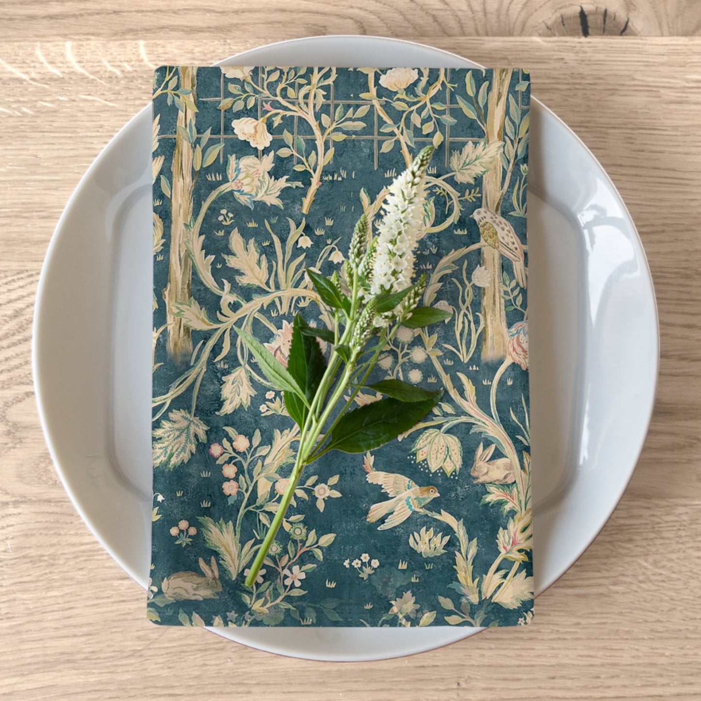 A floral patterned cotton twill napkin in evergreen teal colour, displayed on a plate with a white flower garnish.