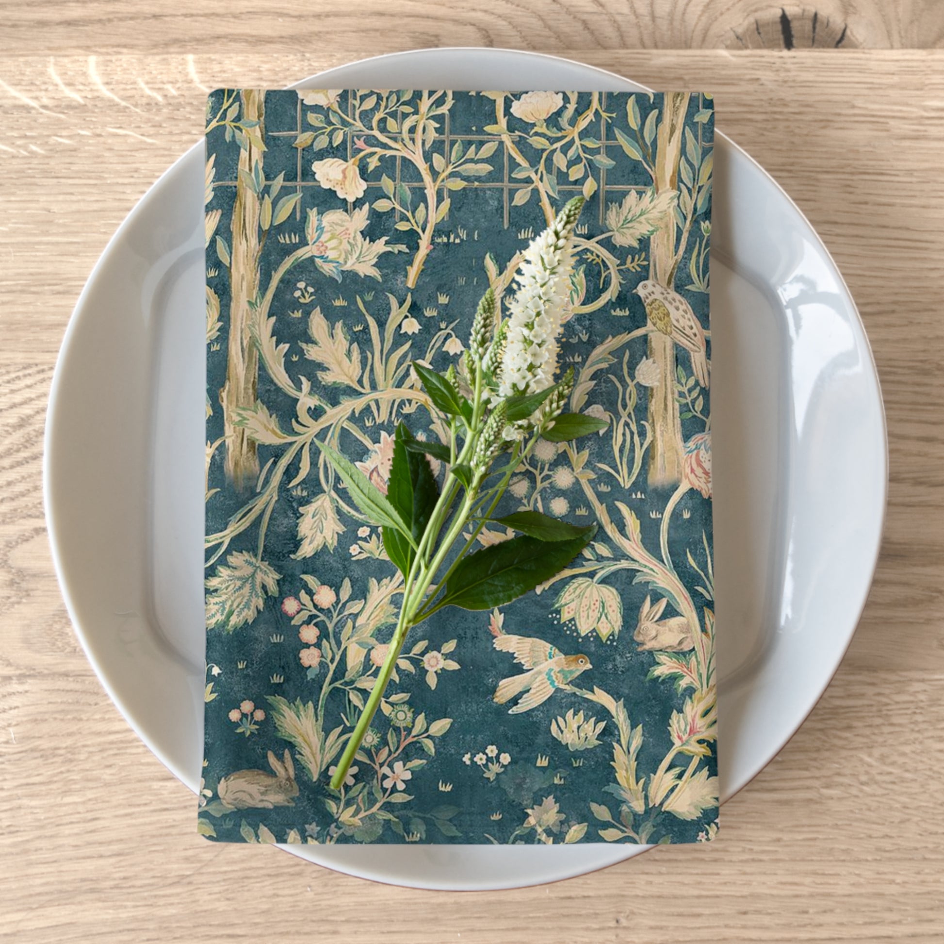 A floral patterned cotton twill napkin in evergreen teal colour, displayed on a plate with a white flower garnish.
