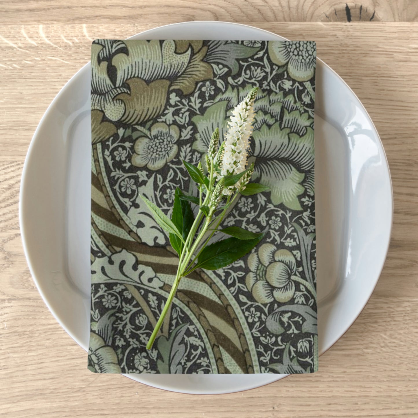 A floral patterned cotton twill napkin inspired by William Morris, displayed on a plate with a piece of floral decor on top.
