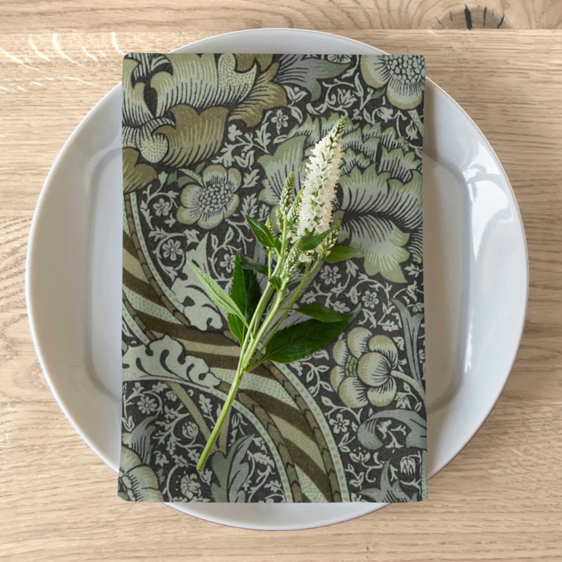 A floral patterned cotton twill napkin inspired by William Morris, displayed on a plate with a piece of floral decor on top.