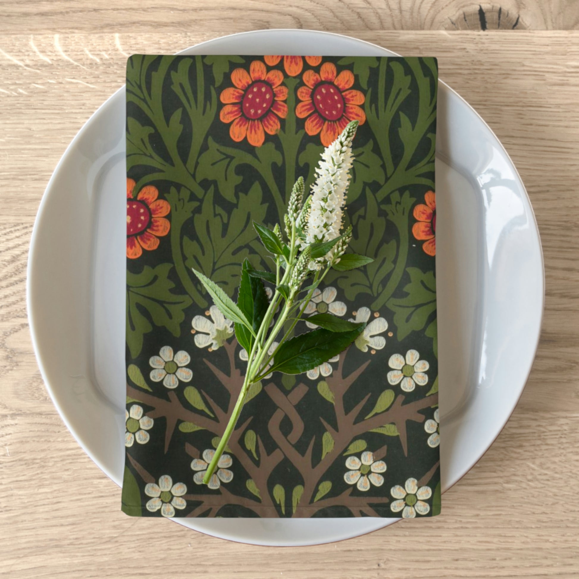 A floral patterned cotton twill napkin inspired by William Morris, displayed on a plate with a plant decoration.