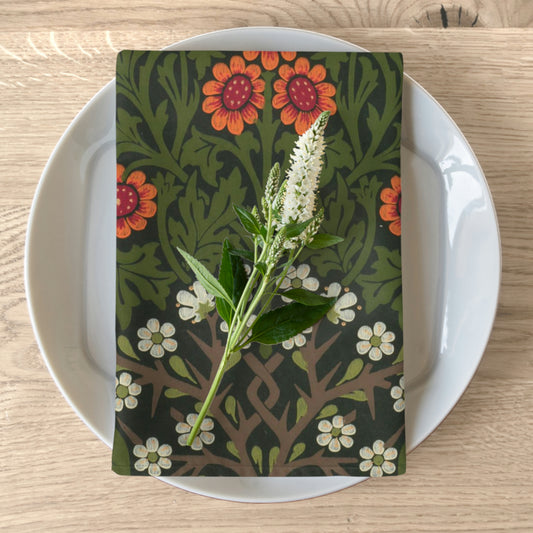 A floral patterned cotton twill napkin inspired by William Morris, displayed on a plate with a plant decoration.