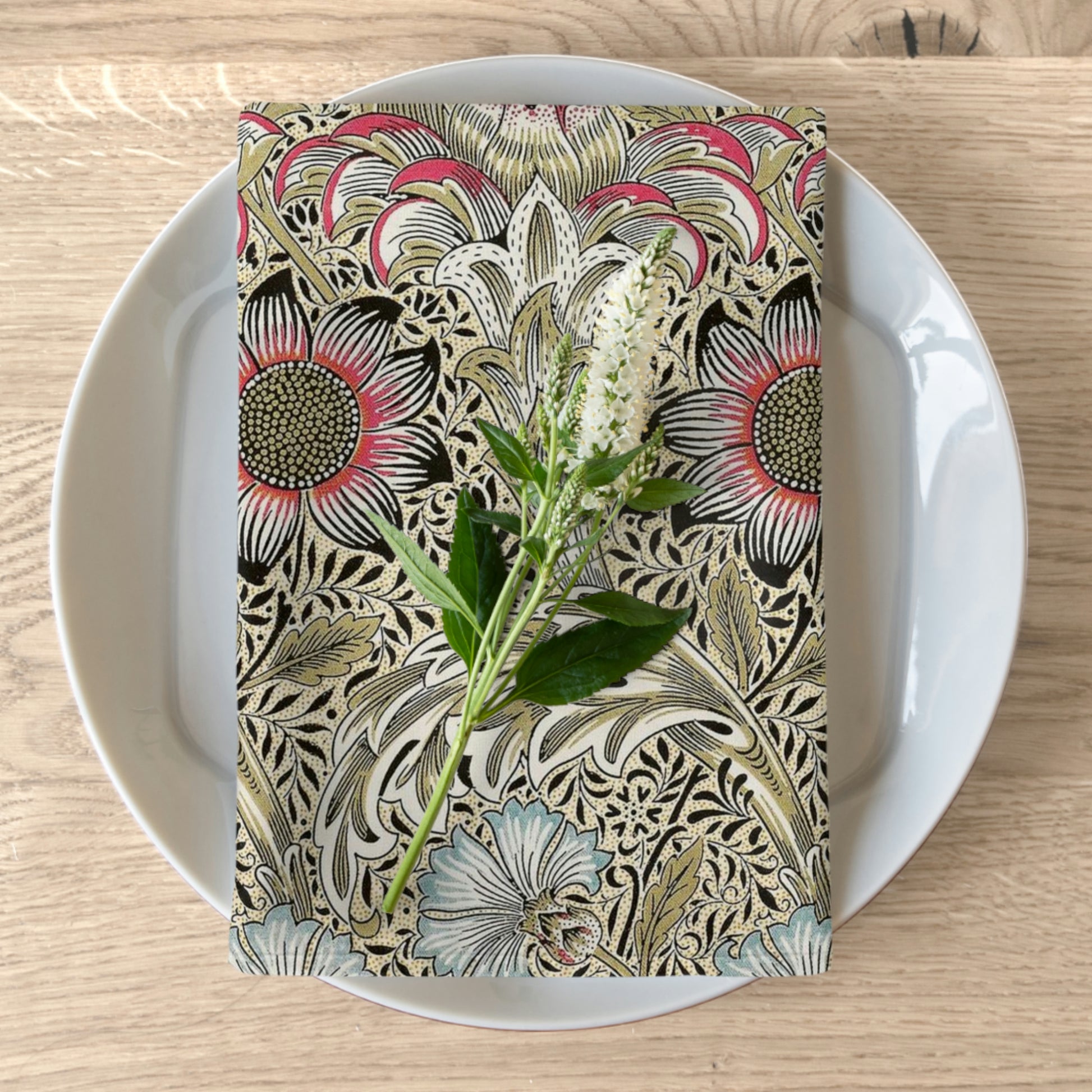 A floral patterned cotton twill napkin inspired by William Morris, displayed on a plate with a piece of floral decor.