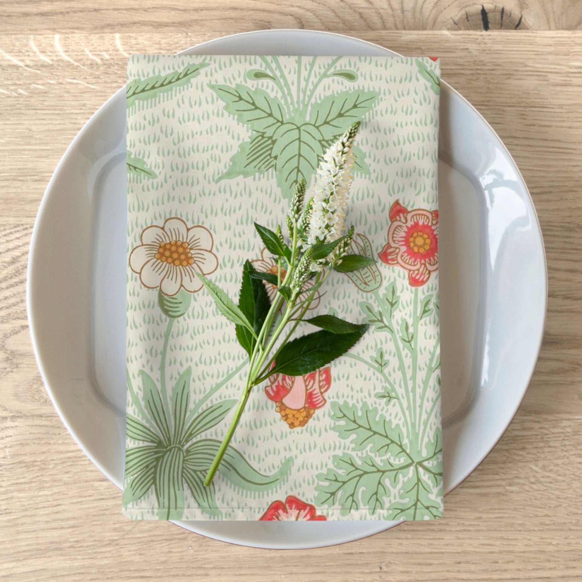 A floral patterned cotton twill napkin inspired by William Morris, displayed on a plate with a piece of floral decor.