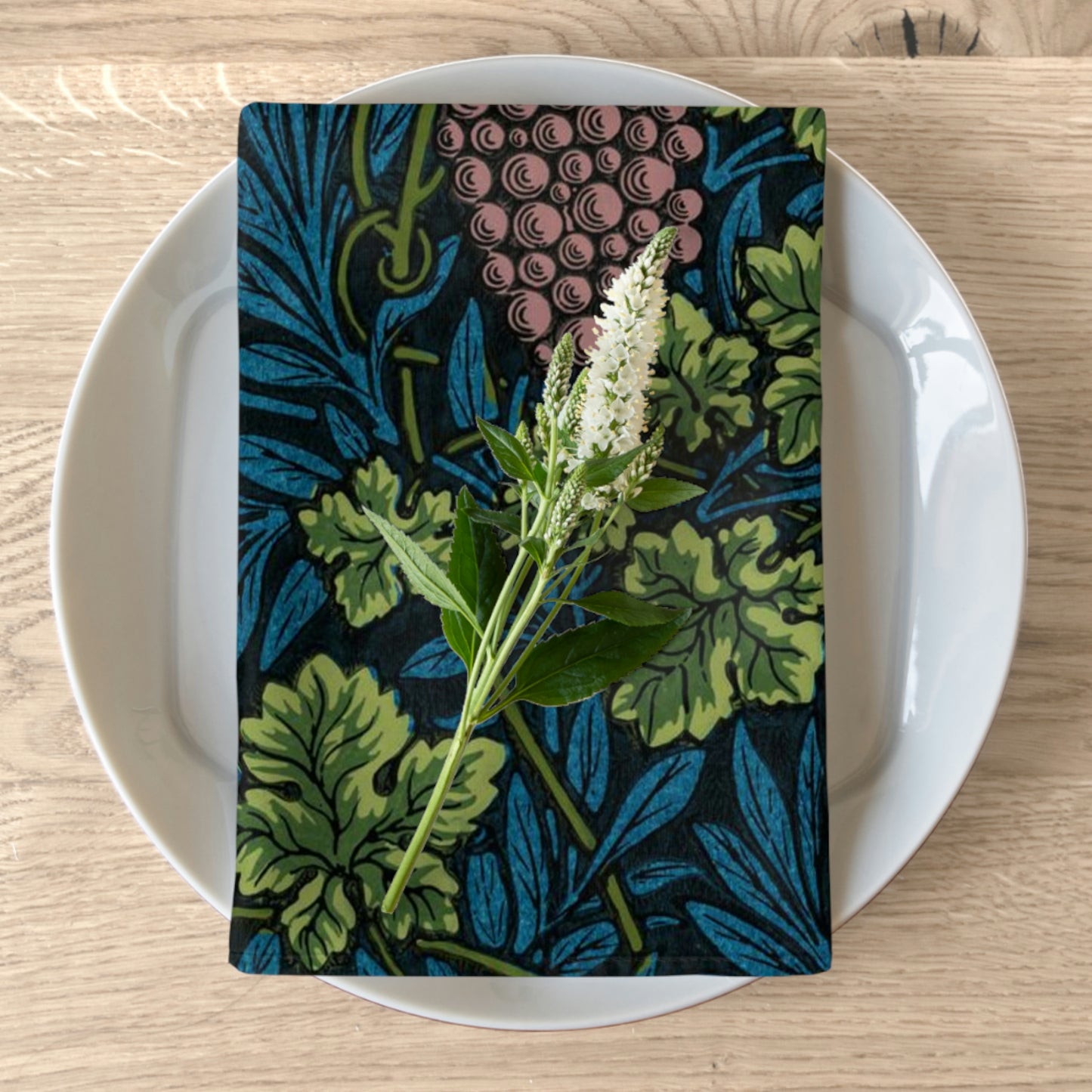 A floral patterned cotton twill napkin on a white plate, with a wooden table in the background.