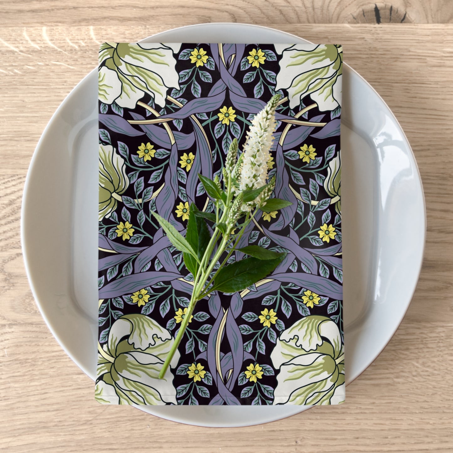 A floral patterned cotton twill napkin inspired by William Morris, displayed on a plate with a white flower decoration.