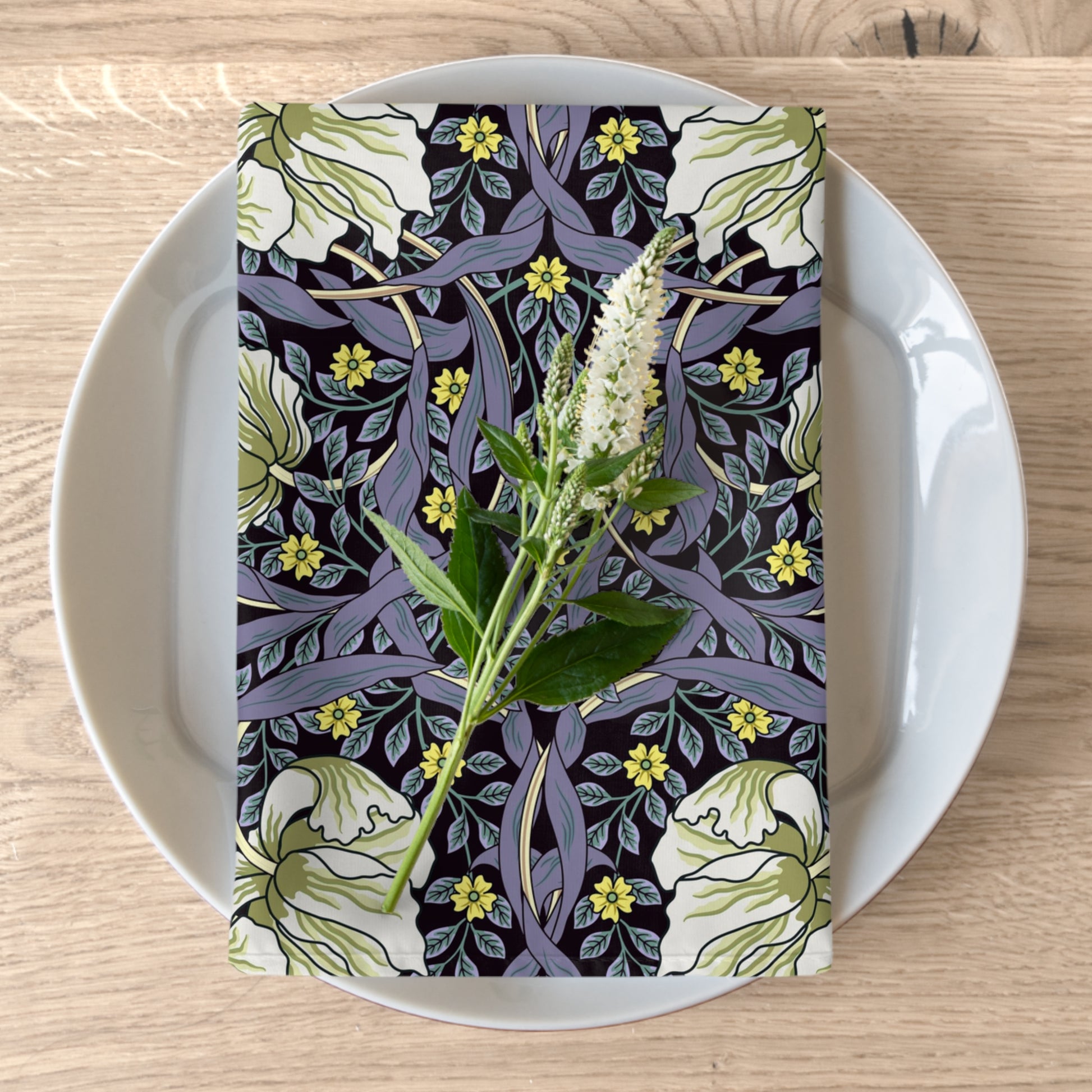 A floral patterned cotton twill napkin inspired by William Morris, displayed on a plate with a white flower decoration.
