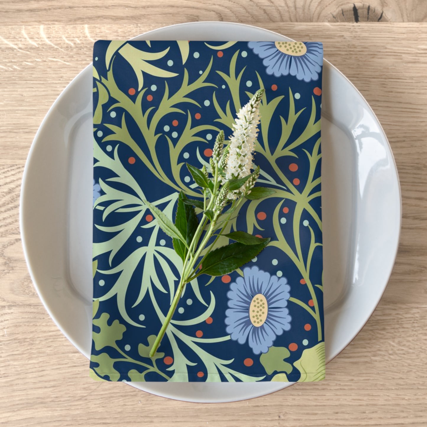 A blue floral patterned cotton twill napkin on a plate, with a seaweed design inspired by William Morris.