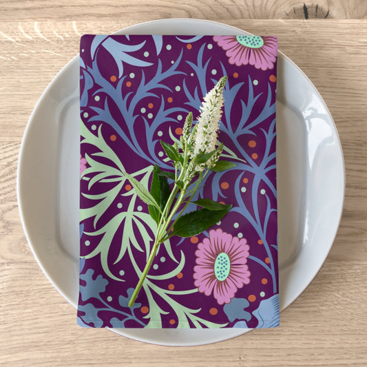 A purple cotton twill napkin with a floral pattern, inspired by William Morris, placed on a plate on a wooden table.