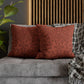 Red patterned pillows on a gray sofa with a wooden headboard and plant in the background