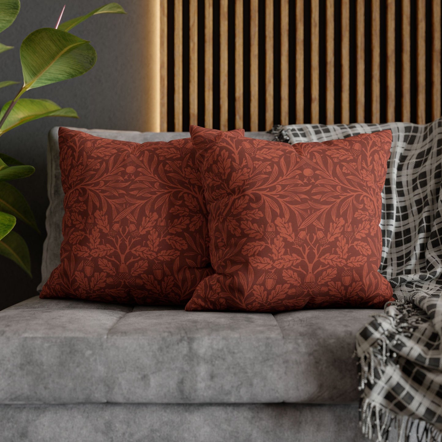Red patterned pillows on a gray sofa with a wooden headboard and plant in the background