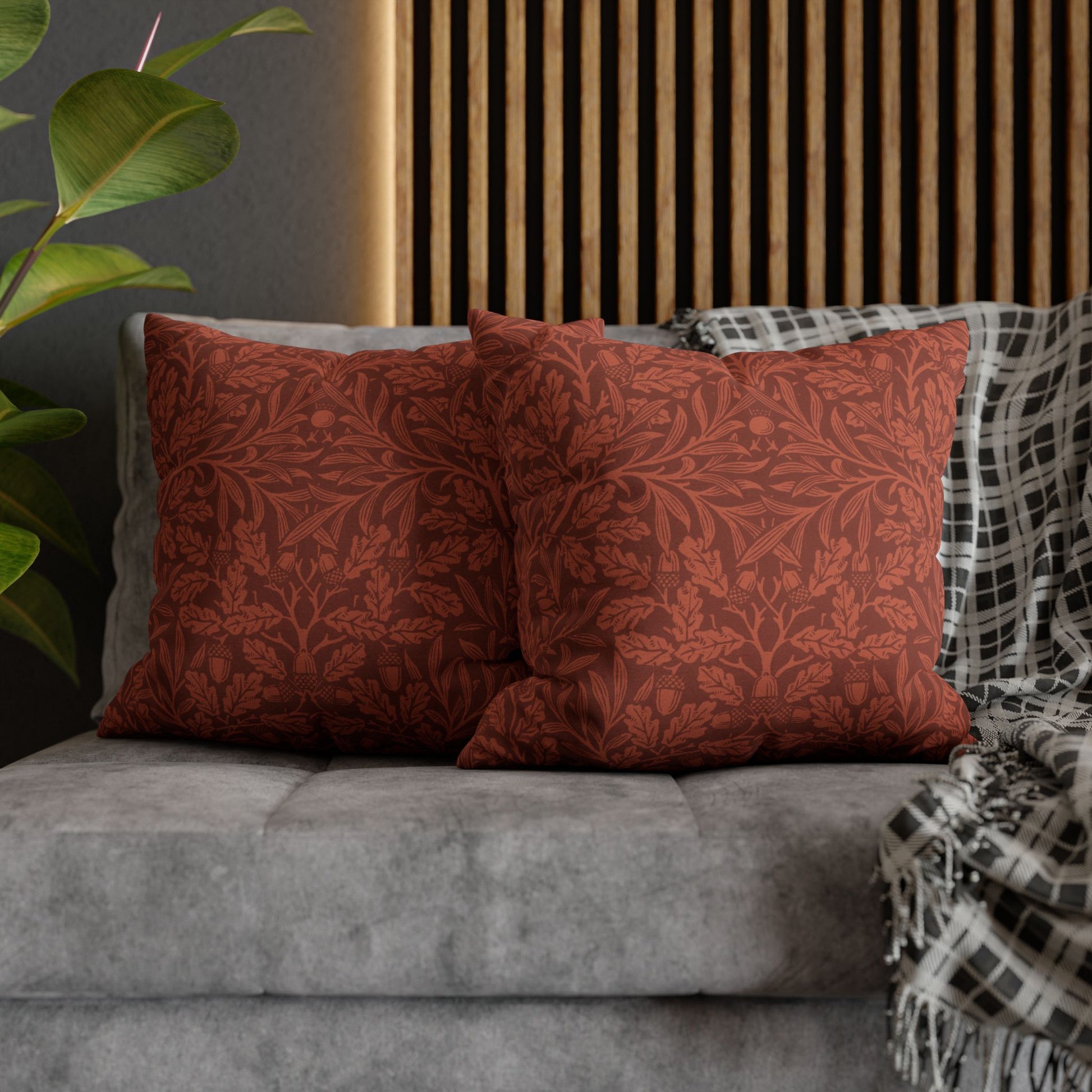 Red patterned pillows on a gray sofa with a wooden headboard and plant in the background