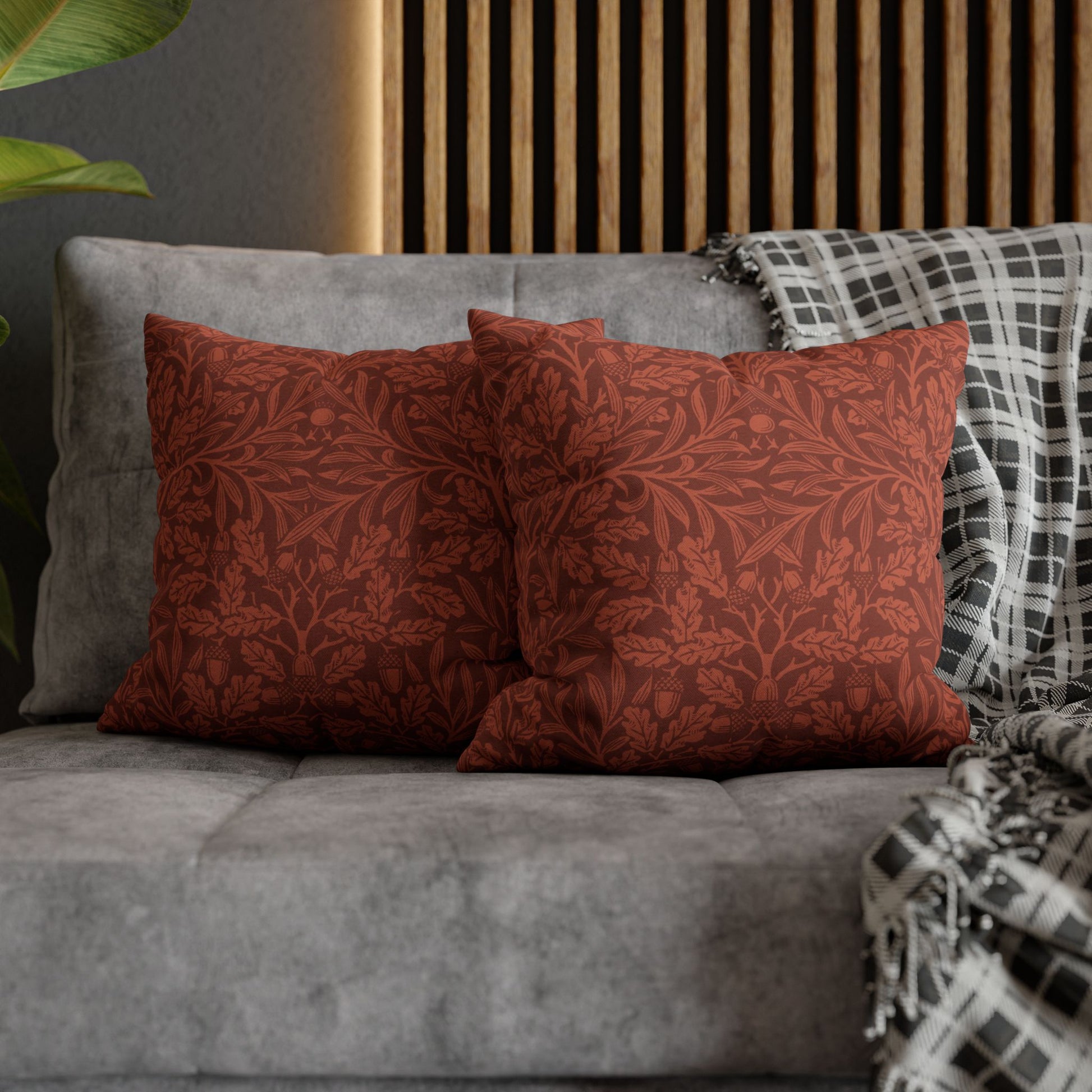 Two red patterned pillows on a gray sofa with a wooden headboard in the background.