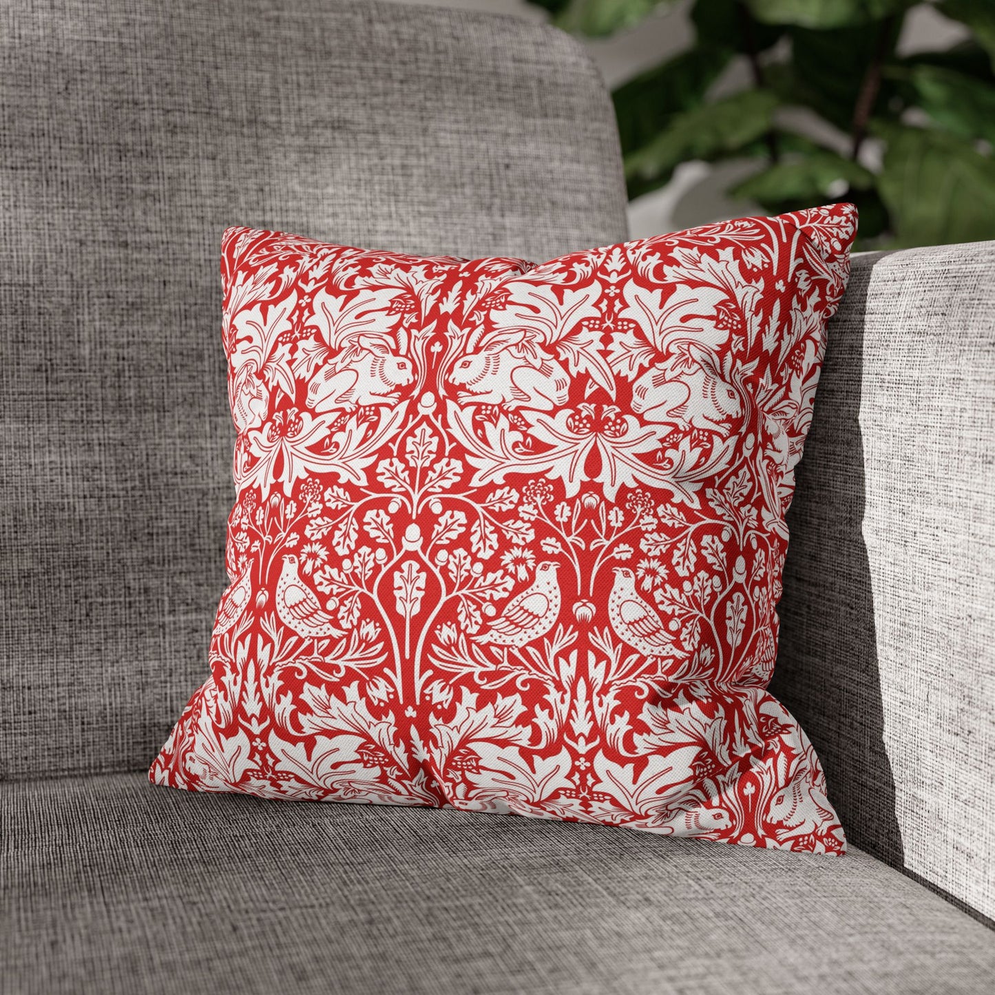 Red and white patterned pillow on a gray couch with a blurred green plant background