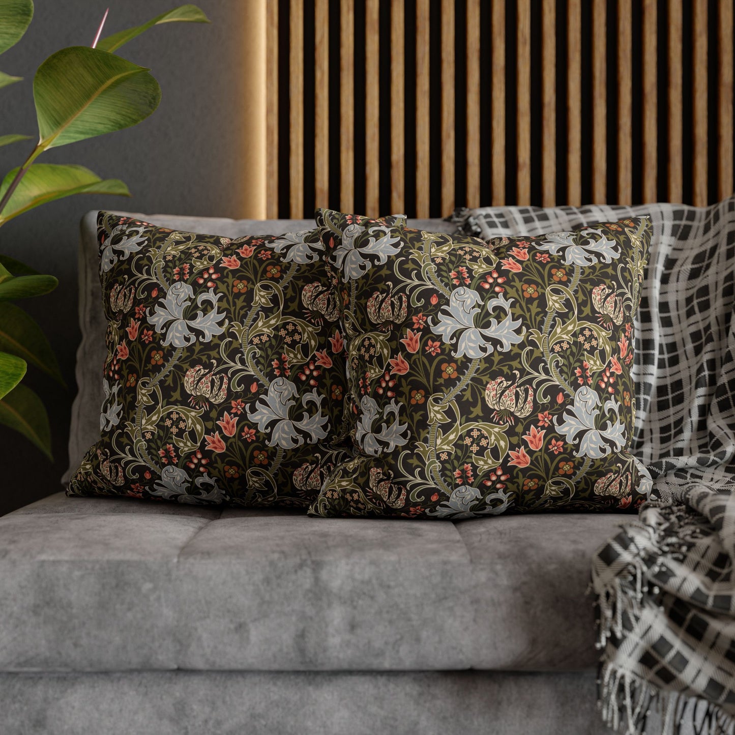 Floral patterned pillows on a gray sofa with a plant and wooden panel in the background