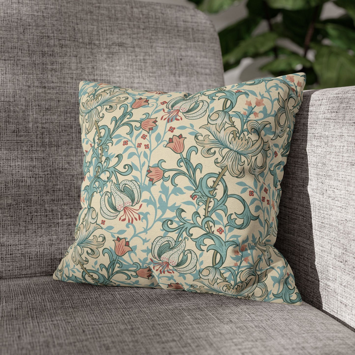 Decorative floral pillow on a gray sofa with a blurred green plant in the background
