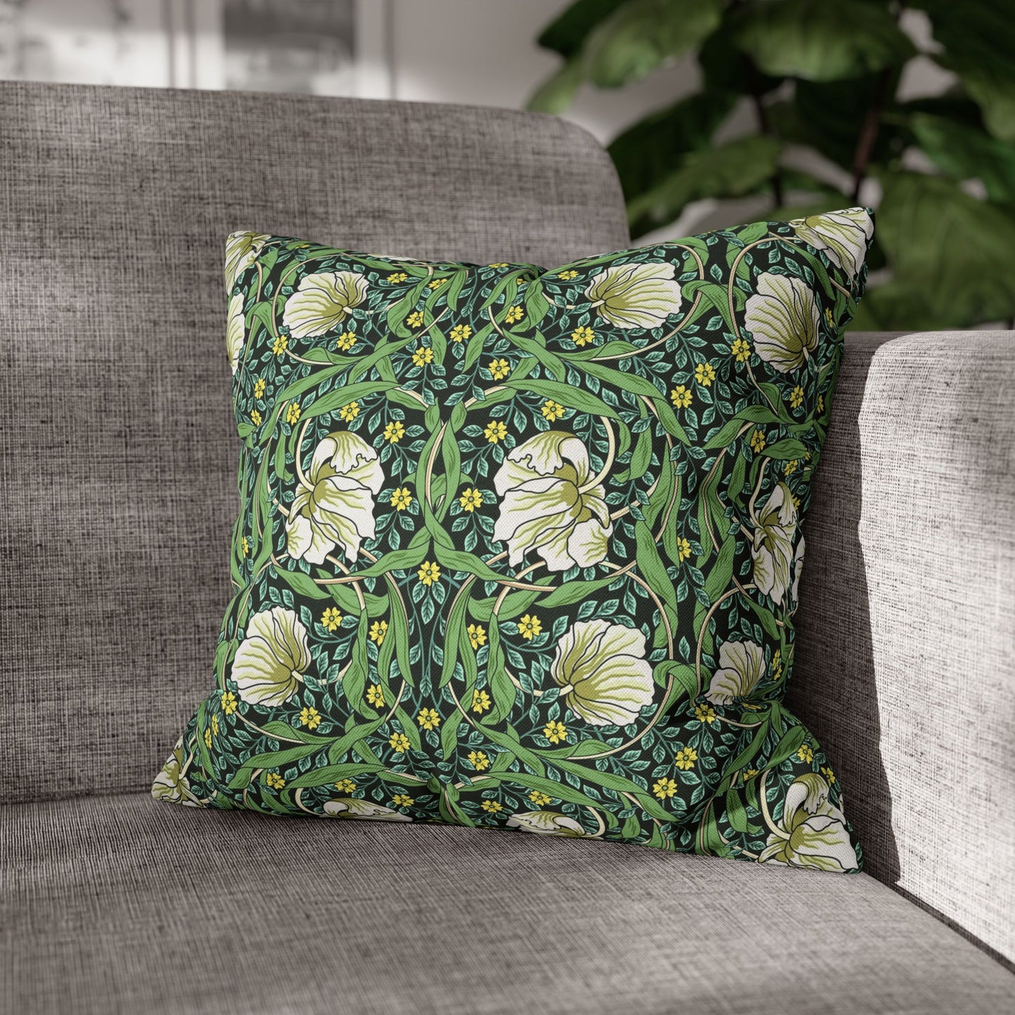 Floral patterned pillow on a gray sofa with a blurred plant in the background
