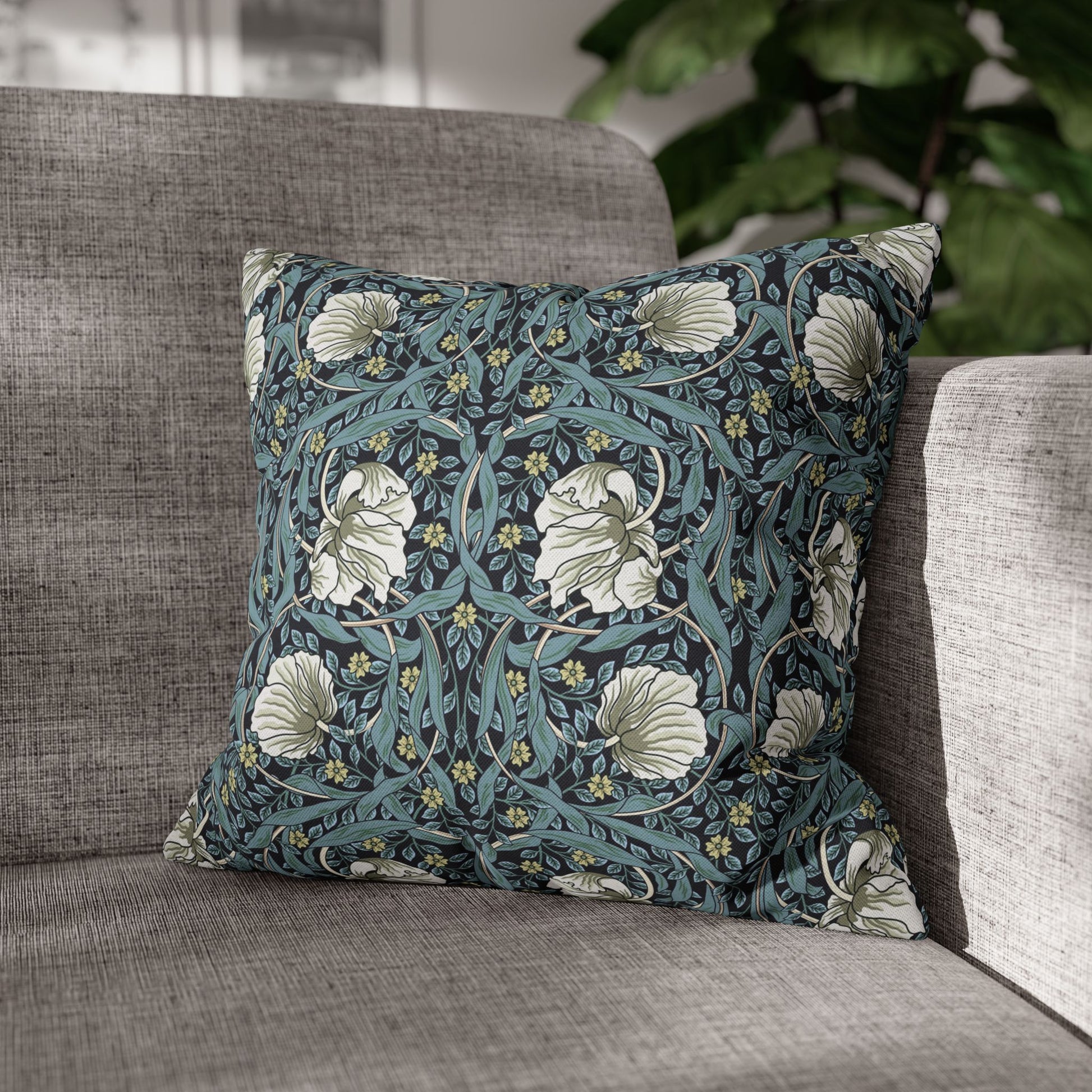 Floral patterned pillow on a gray sofa with a blurred plant in the background