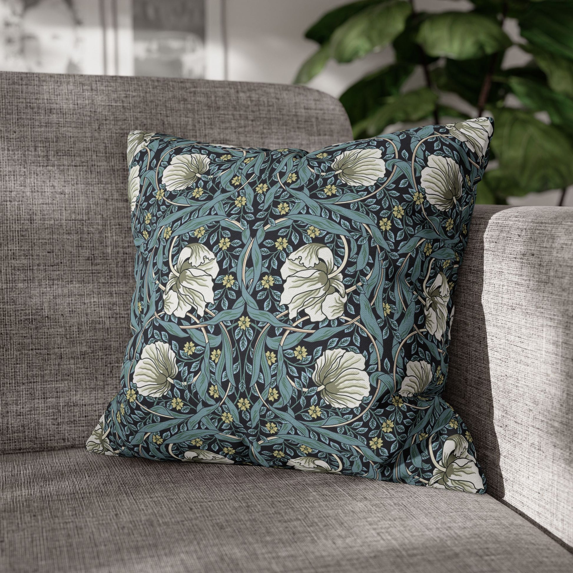 Floral patterned pillow on a gray sofa with a blurred plant in the background