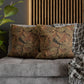Decorative pillows with floral patterns on a gray sofa next to a plant and plaid blanket.