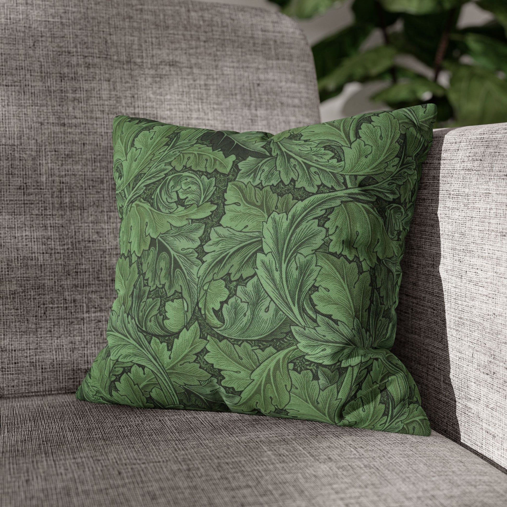 Green leaf-patterned pillow on a gray couch with a blurred plant in the background