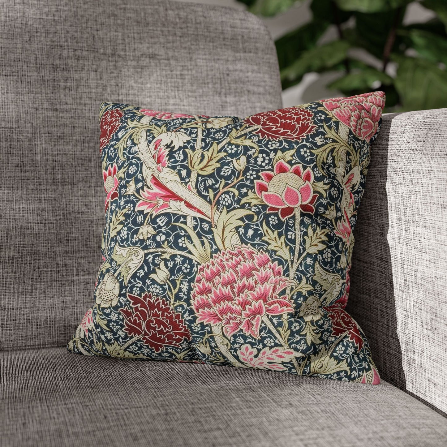Floral patterned pillow on a gray sofa with a blurred green plant background