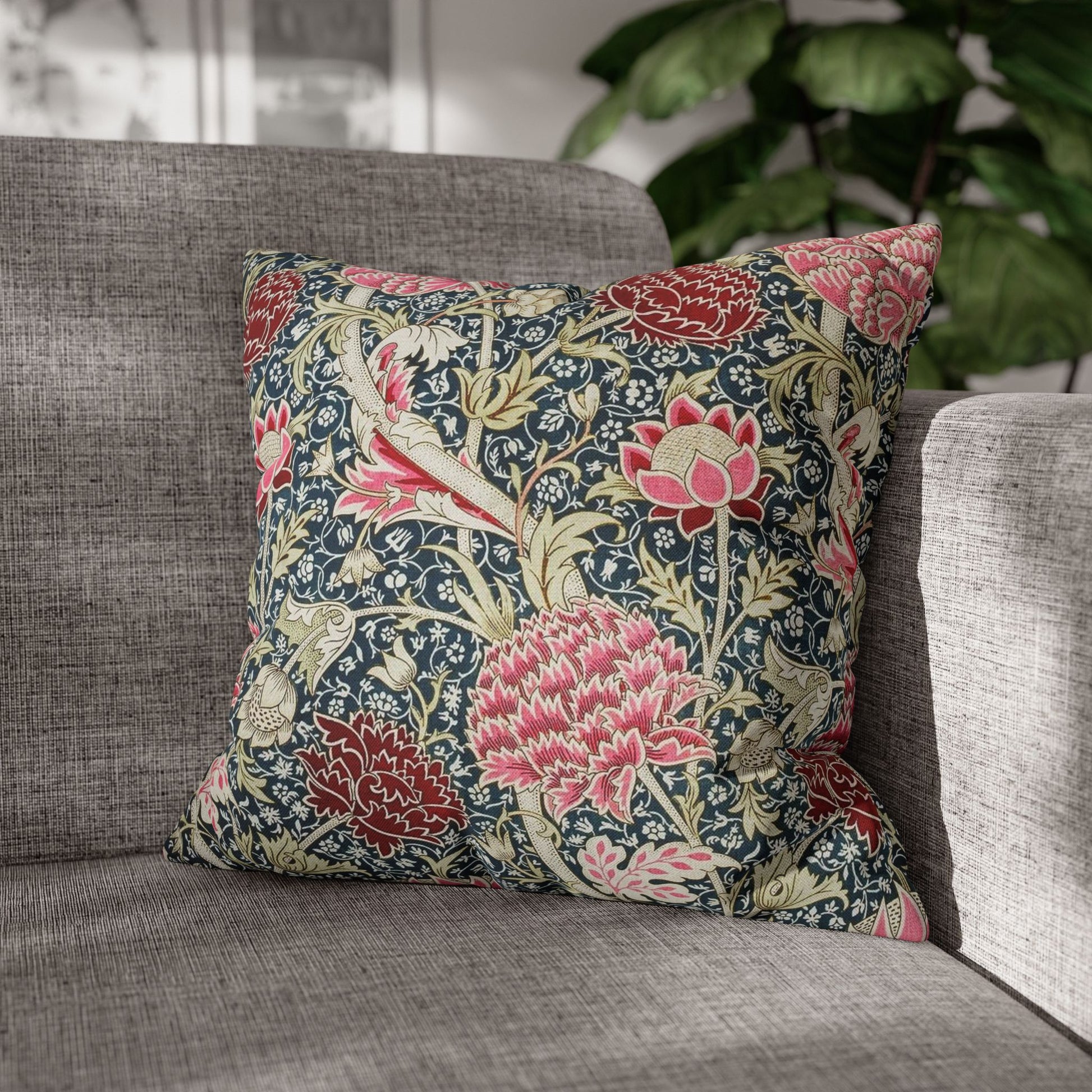 Decorative floral pillow on a gray sofa with a blurred plant in the background