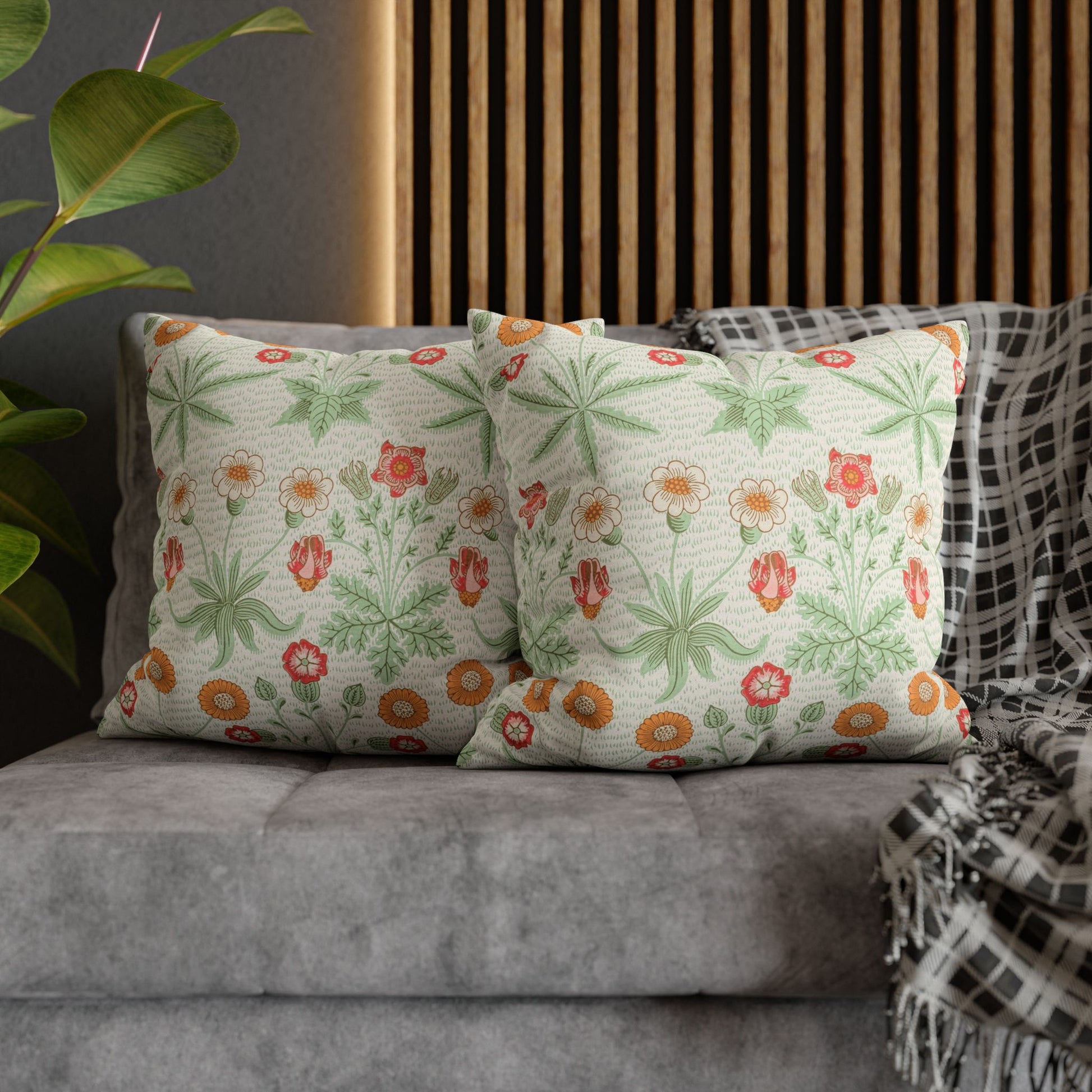 Floral patterned cushions on a gray sofa with a wooden headboard and plant in the background.