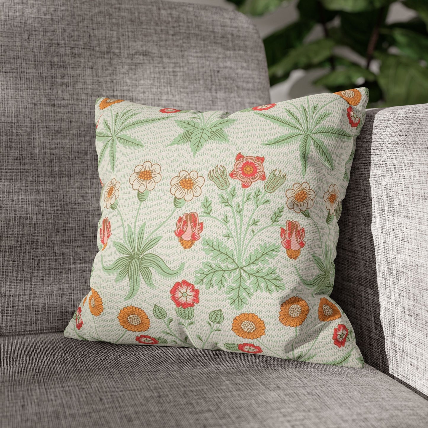 Floral patterned pillow on a gray couch with greenery in the background