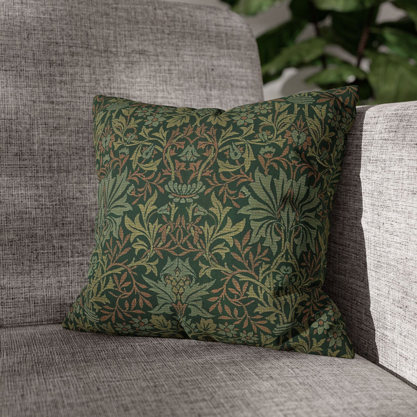 Green patterned pillow on a gray sofa with a blurred plant in the background