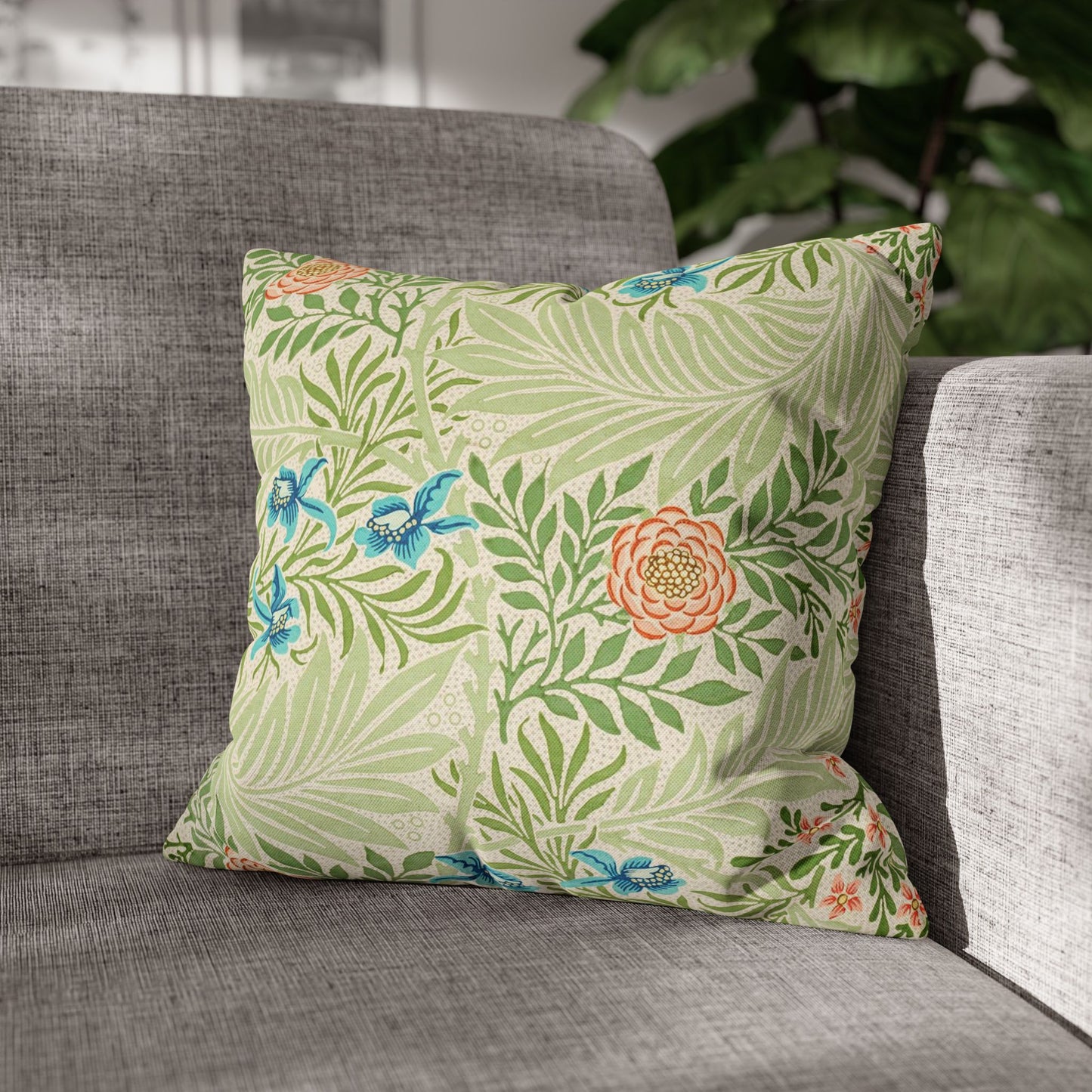 Floral patterned pillow on a gray sofa with a blurred plant in the background