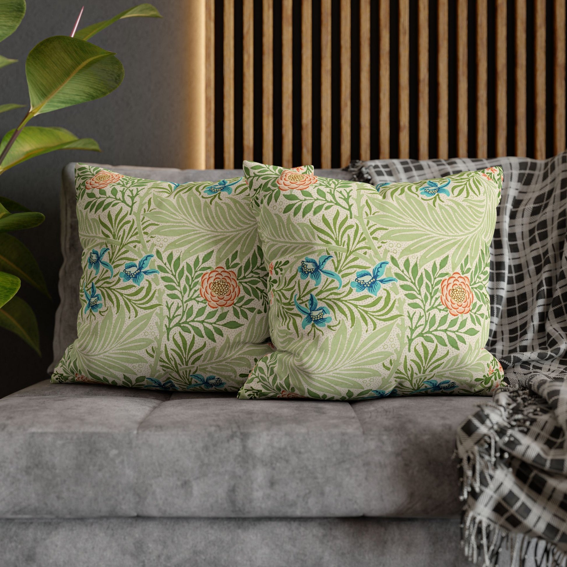 Floral patterned pillows on a gray sofa with a wooden headboard and plant in the background