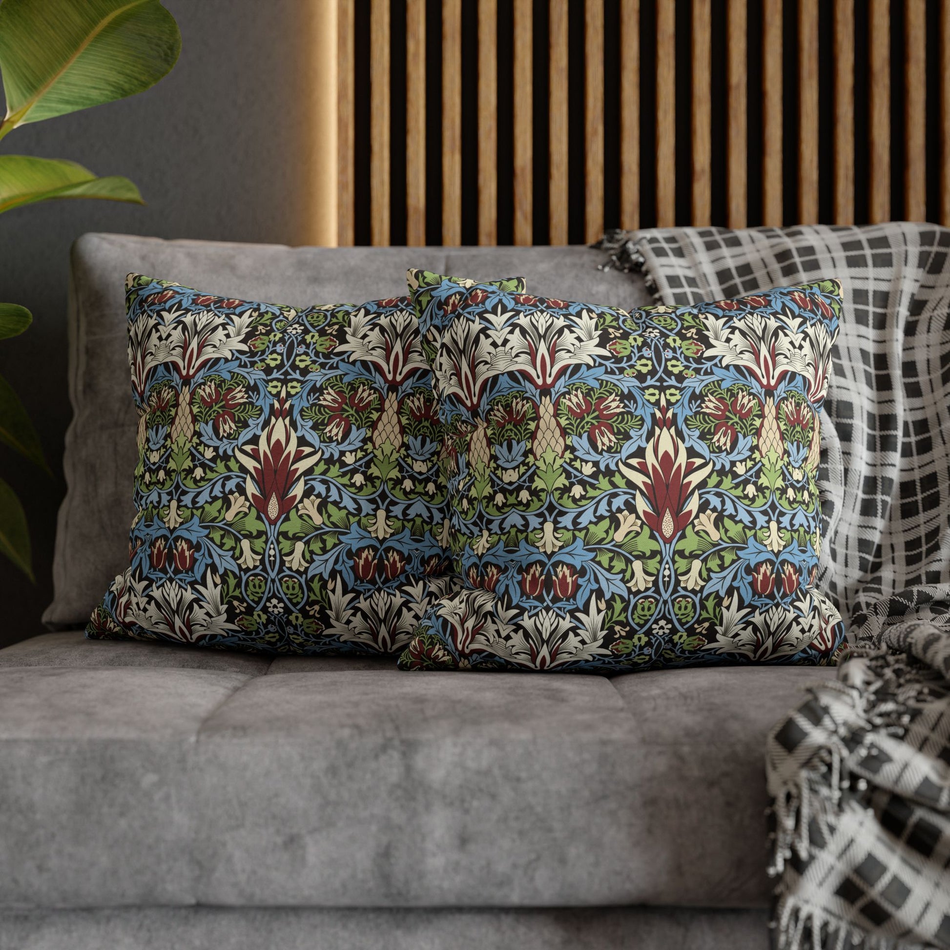 Decorative pillows with a floral pattern on a gray sofa against a wooden panel wall - William Morris Snakeshead