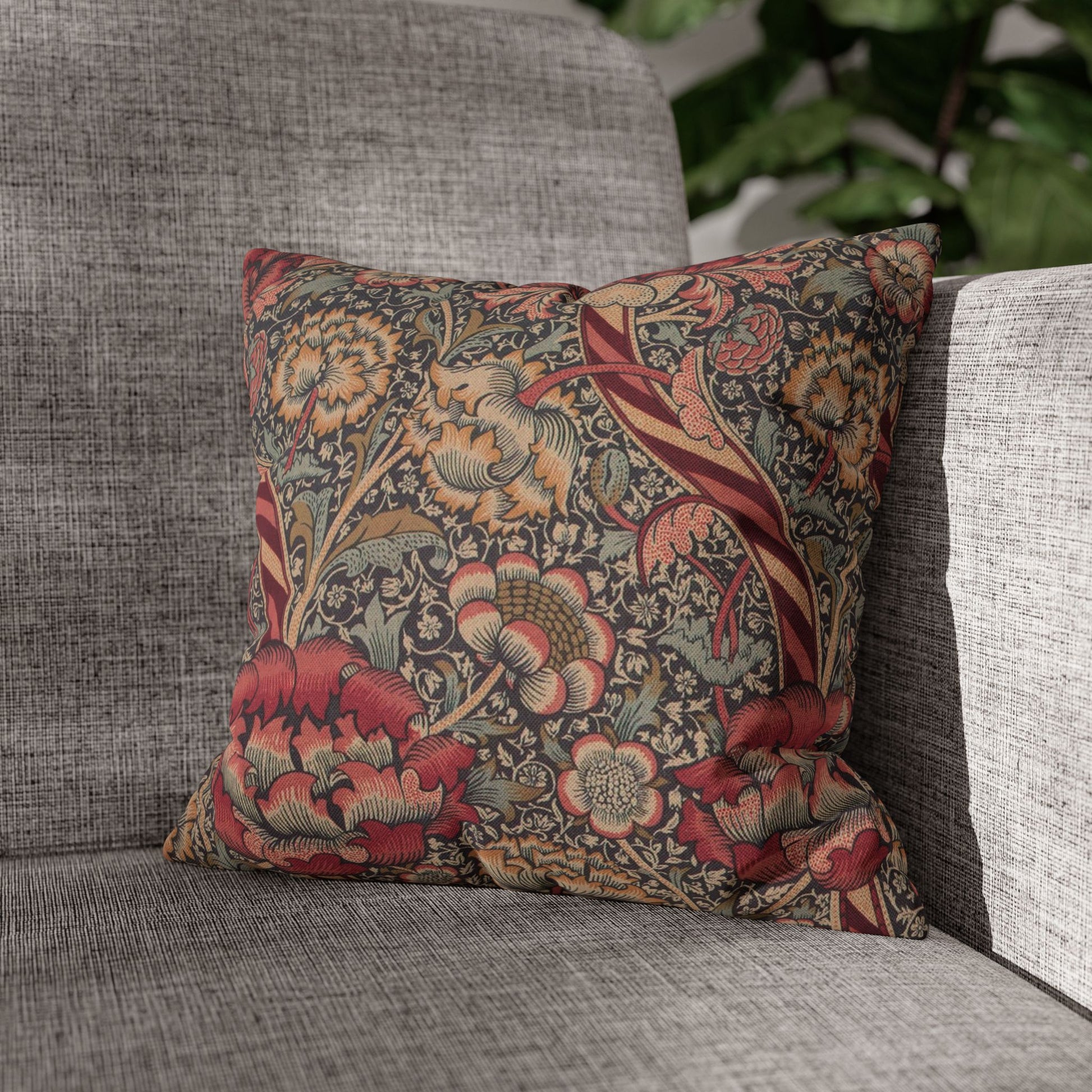 Decorative floral pillow on a gray sofa with a blurred green plant in the background