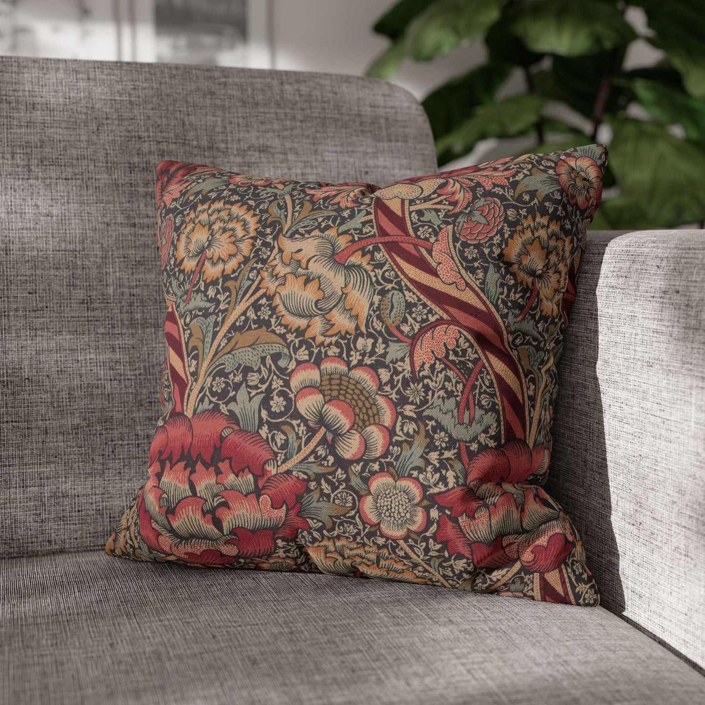 Decorative floral pillow on a gray sofa with a blurred plant in the background