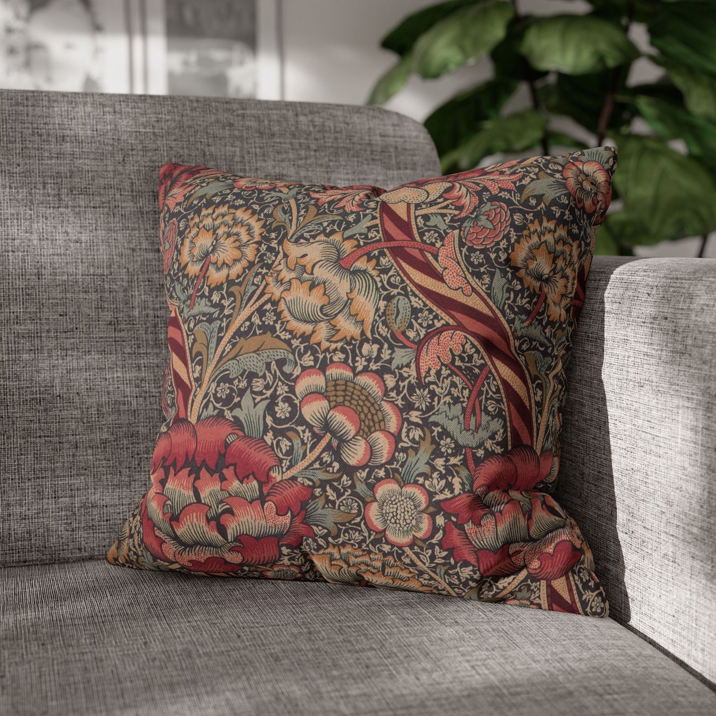 Floral patterned pillow on a gray sofa with a blurred plant in the background