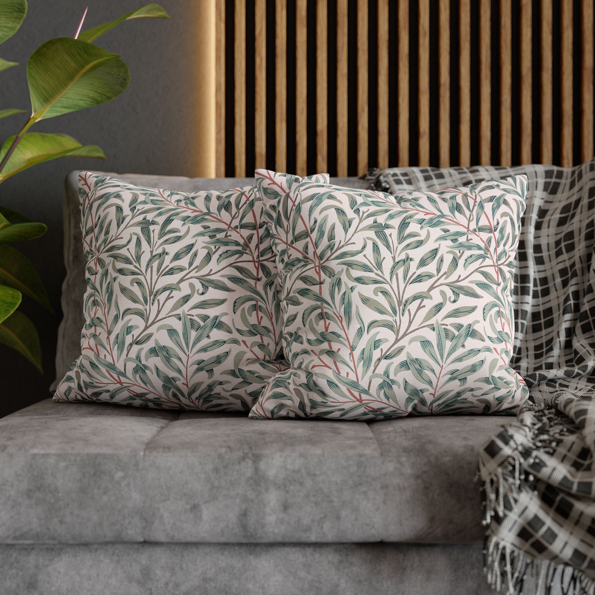 Decorative pillows with leaf patterns on a gray sofa against a wooden slat wall.