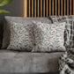 Decorative pillows with leaf patterns on a gray sofa against a wooden headboard.