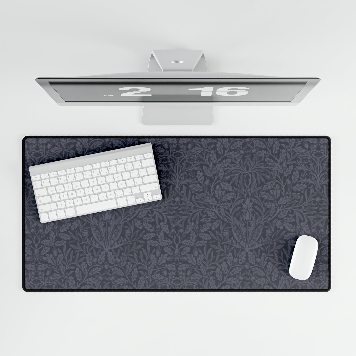 A large desk mat with an acorn and oak leaf pattern in smokey blue, displayed on a desk with a keyboard and mouse.
