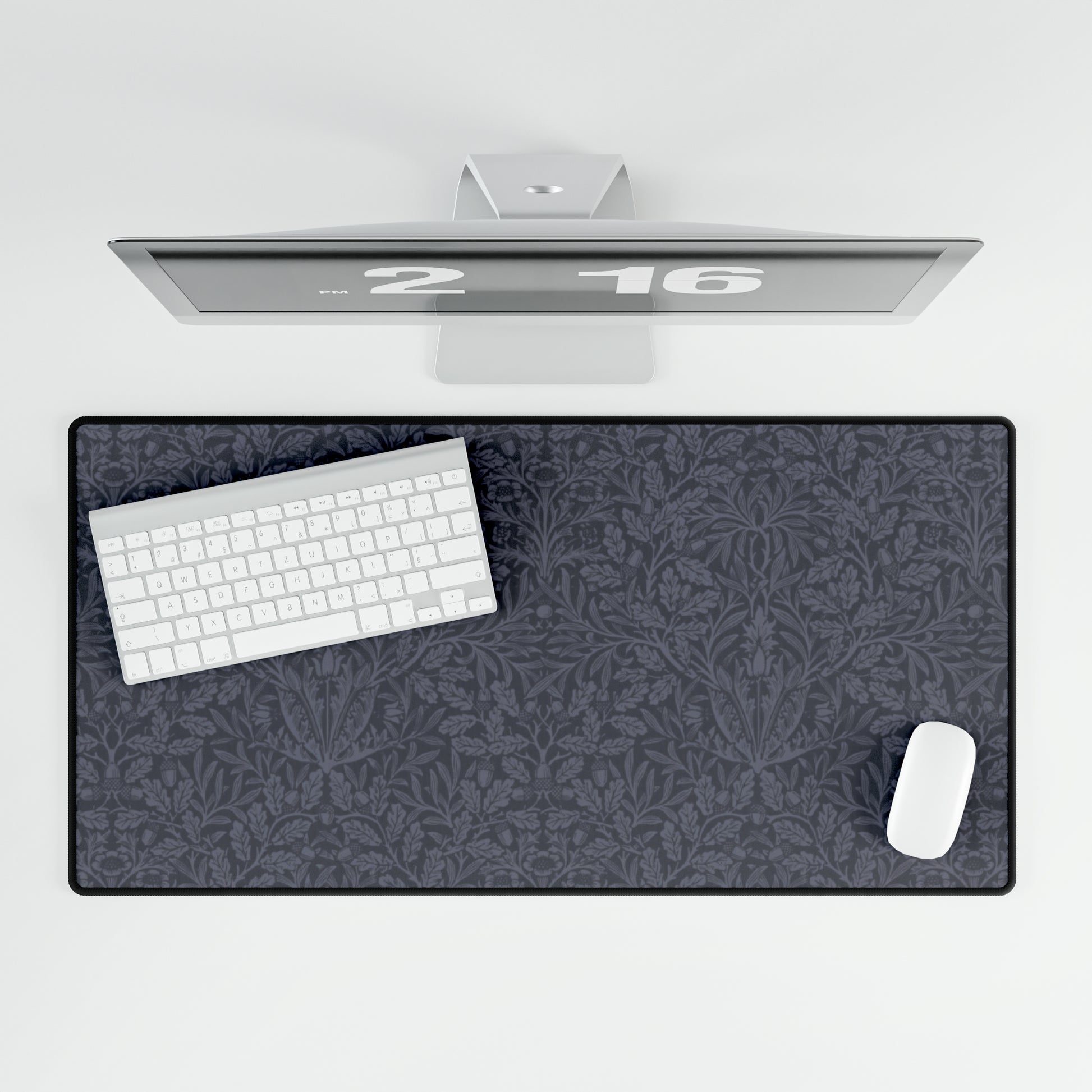 A large desk mat with an acorn and oak leaf pattern in smokey blue, displayed on a desk with a keyboard and mouse.