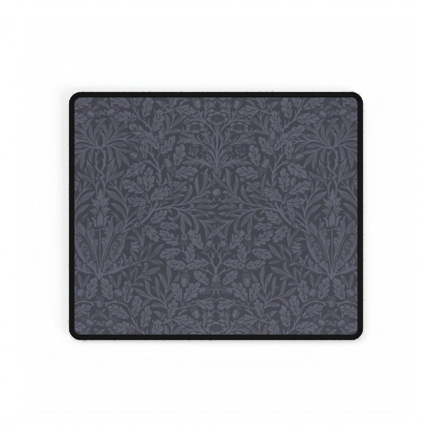 A large desk mat with an acorn and oak leaf pattern in smokey blue, displayed on a desk with a keyboard and mouse.