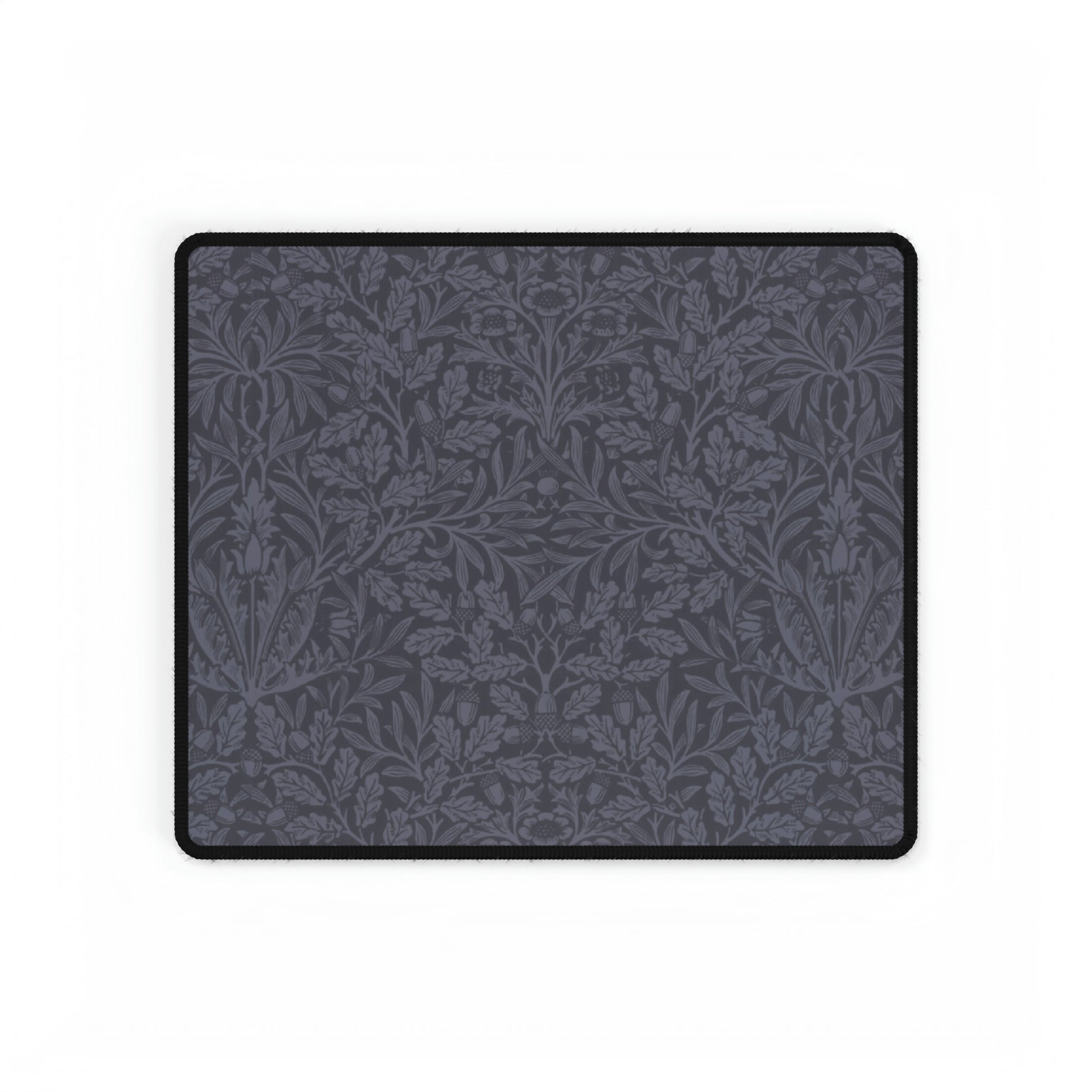A large desk mat with an acorn and oak leaf pattern in smokey blue, displayed on a desk with a keyboard and mouse.