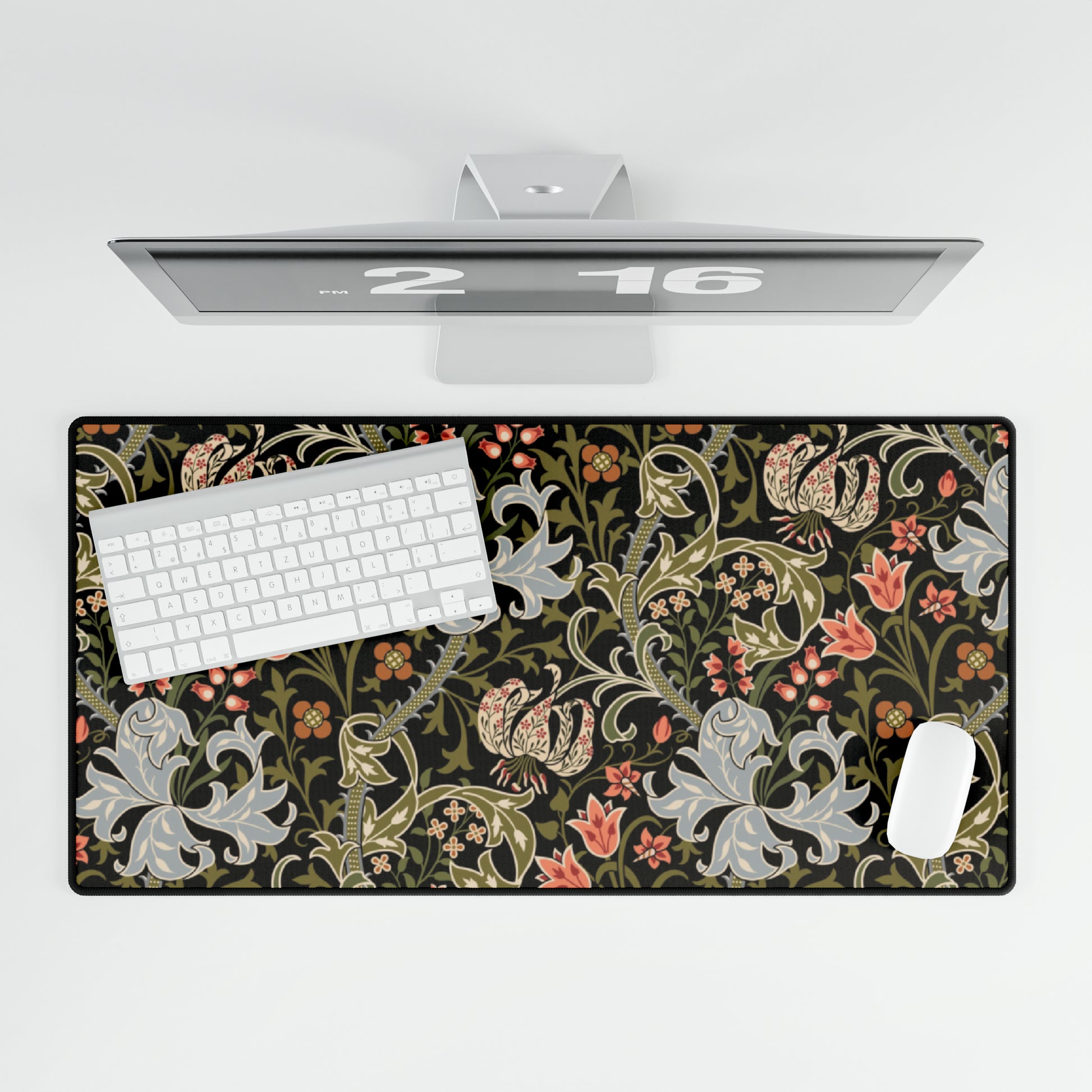 A rectangular desk mat with a William Morris & Co floral pattern in multiple colours, placed under a desk with a keyboard and mouse on top.