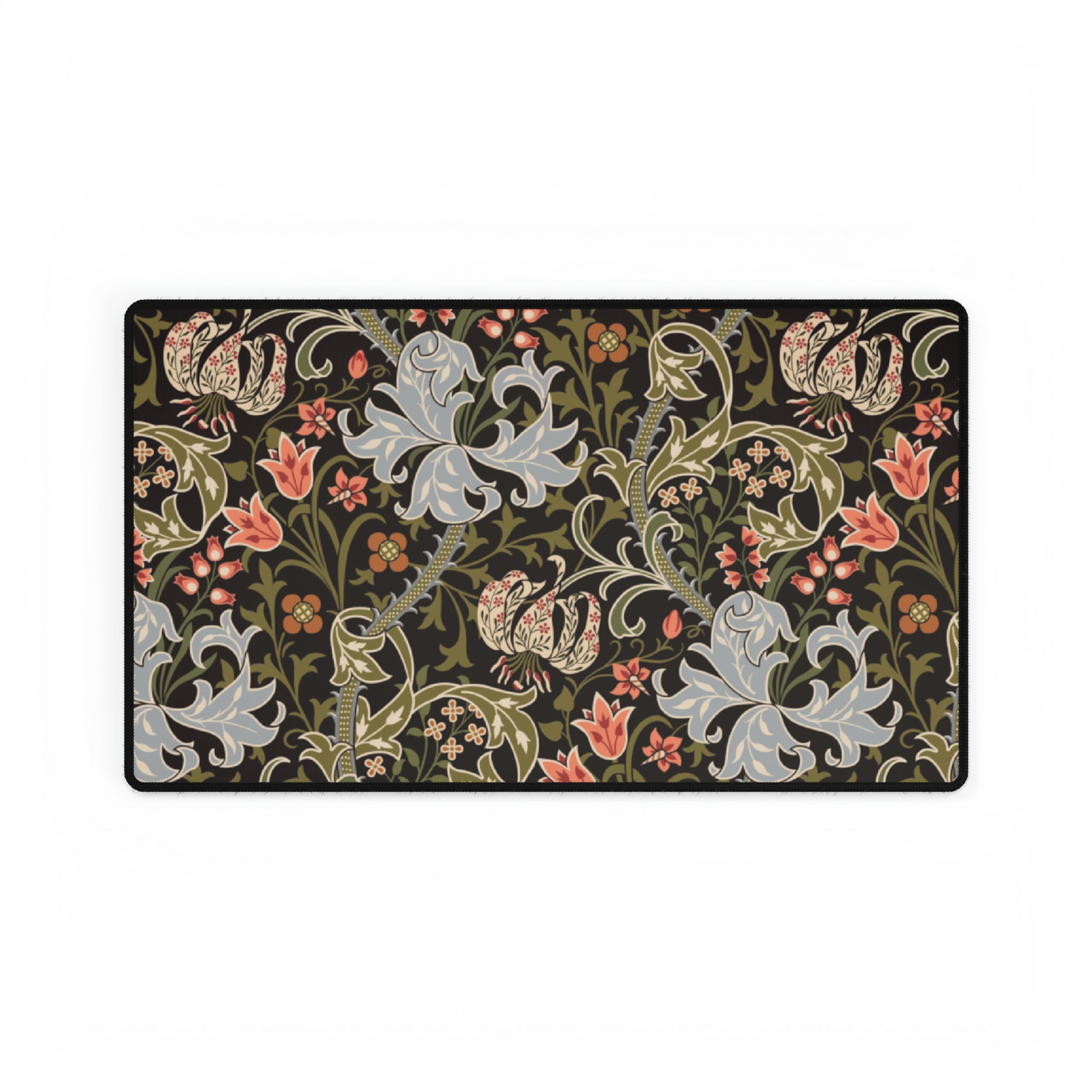 A rectangular desk mat with a William Morris & Co floral pattern in multiple colours, placed under a desk with a keyboard and mouse on top.
