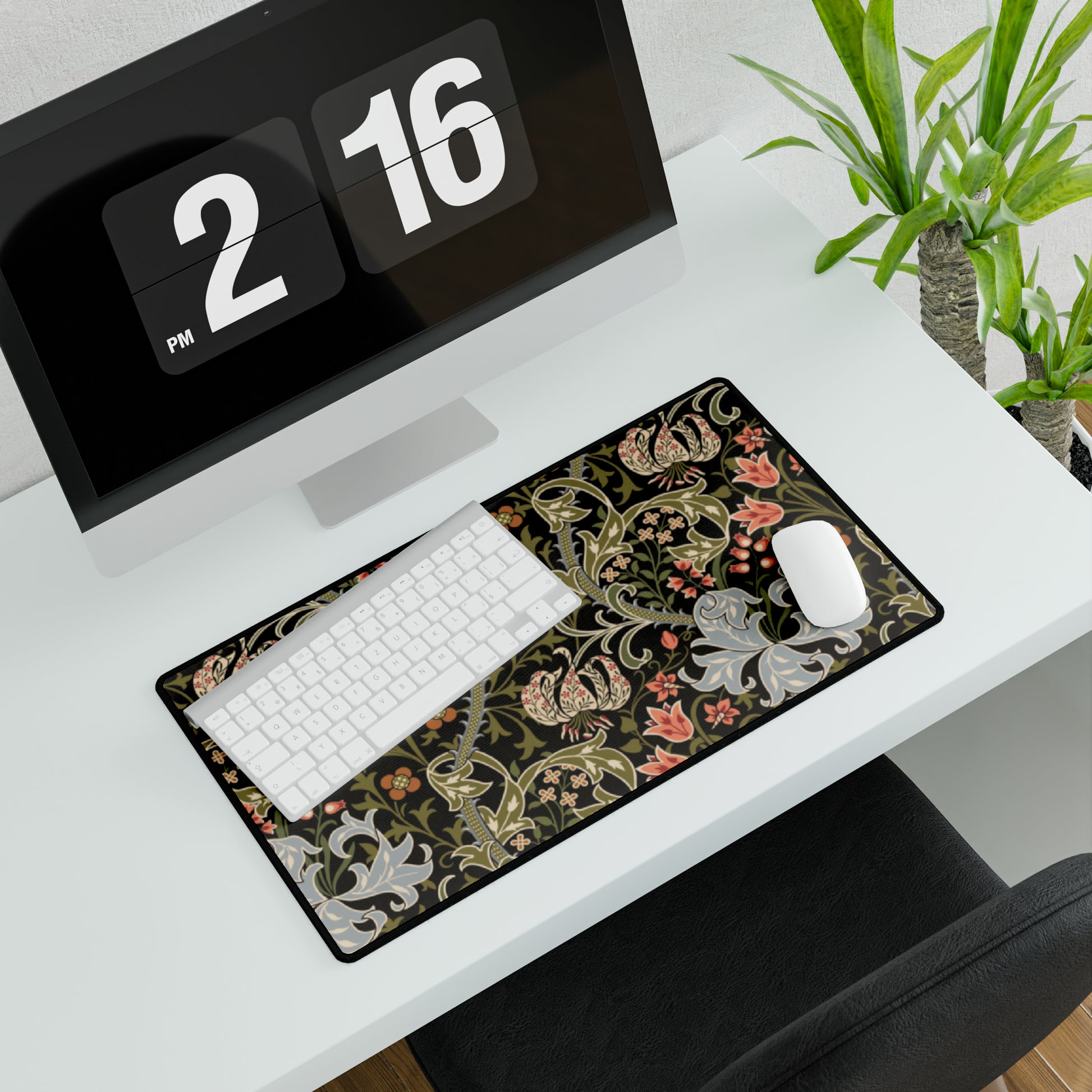 A rectangular desk mat with a William Morris & Co floral pattern in multiple colours, placed under a desk with a keyboard and mouse on top.