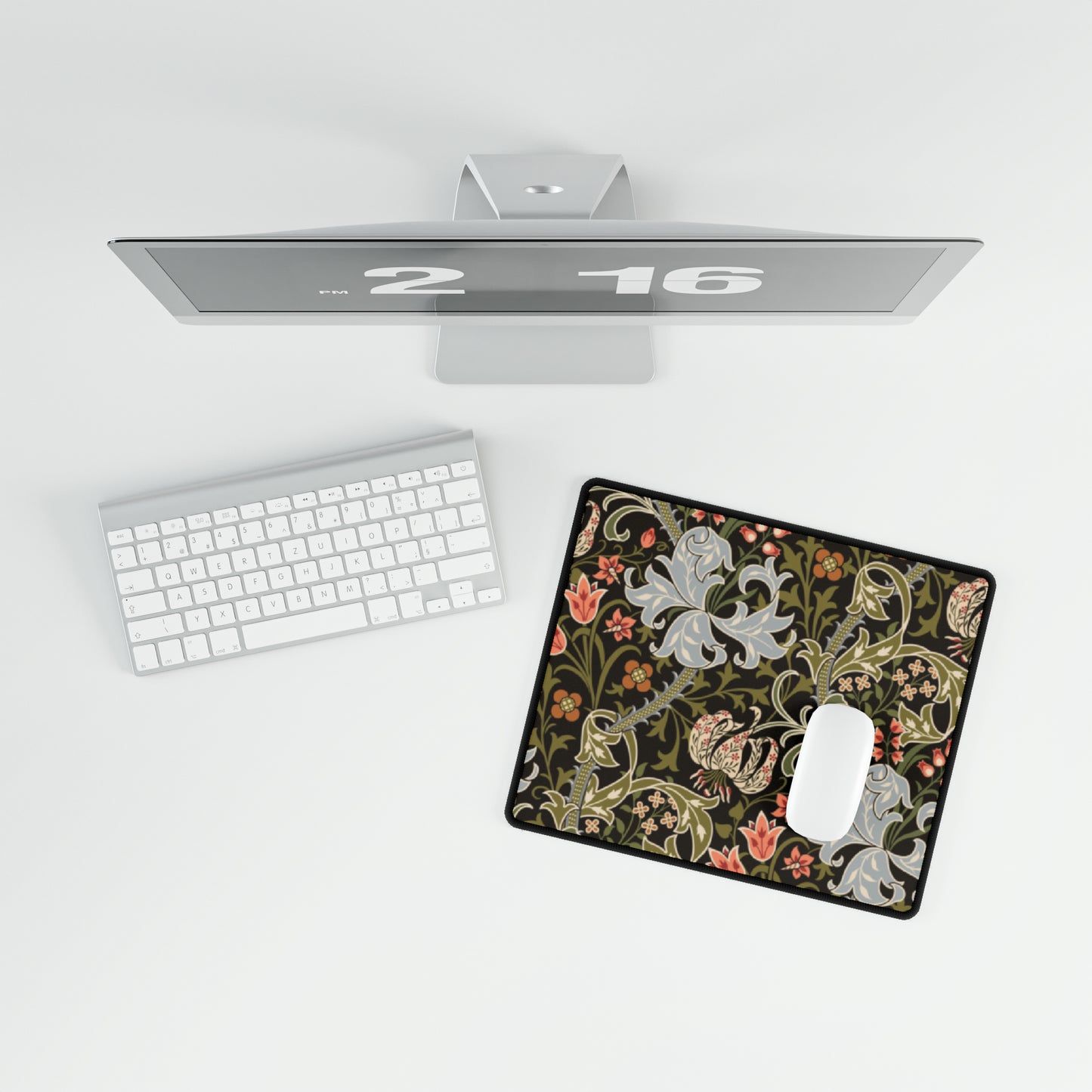 A rectangular desk mat with a William Morris & Co floral pattern in multiple colours, placed under a desk with a keyboard and mouse on top.