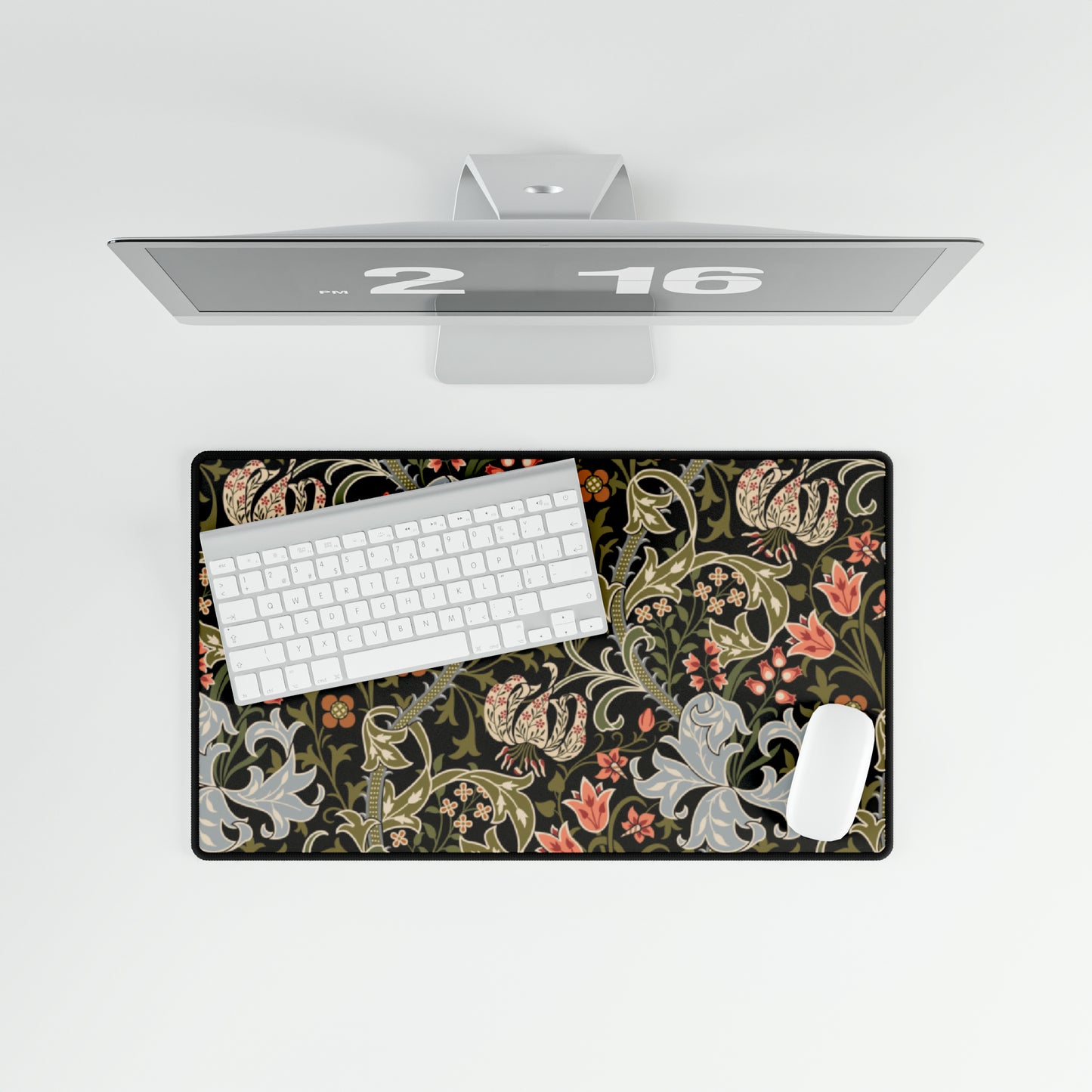 A rectangular desk mat with a William Morris & Co floral pattern in multiple colours, placed under a desk with a keyboard and mouse on top.